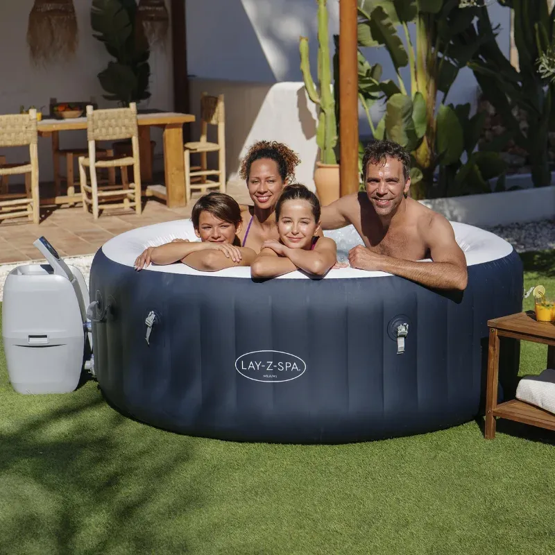 Deux adultes et deux enfants accoudés au rebord du Lay-Z-Spa Miami installé sur une pelouse