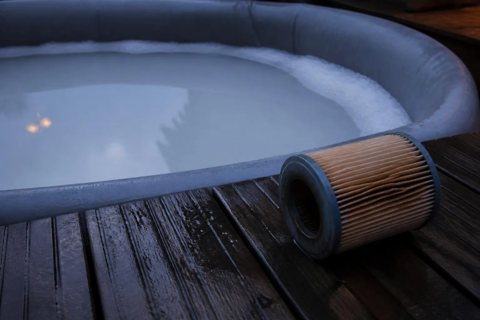 Eau laiteuse et couronne de mousse dans un spa gonflable au crépuscule, cartouche de filtration sortie et posée sur la terrasse