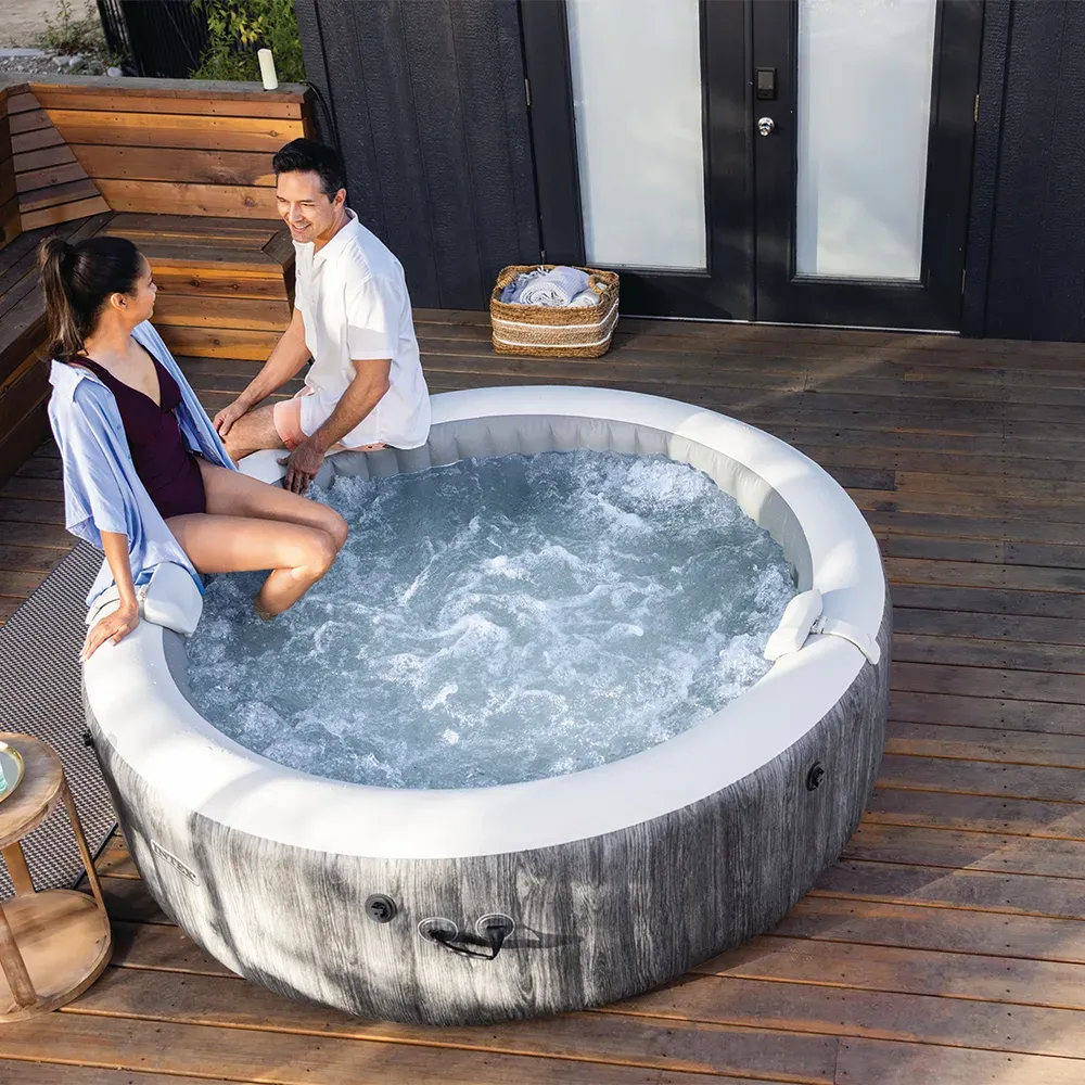 Deux adultes assis sur le rebord du spa Intex Baltik installé sur une terrasse en bois