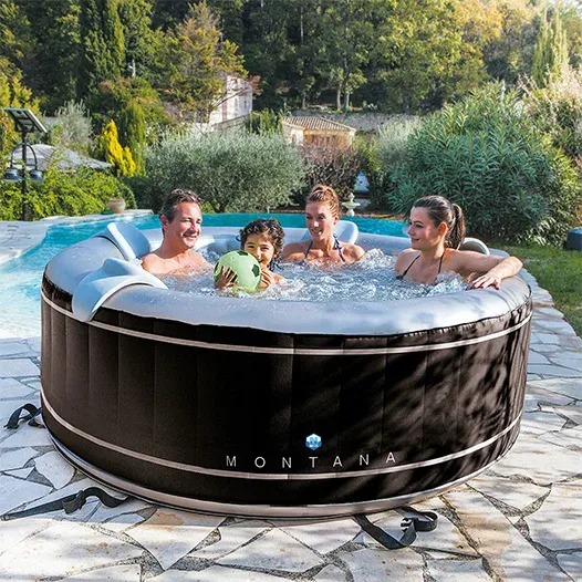Trois adultes et un enfant dans le NetSpa Montana installé sur une terrasse en pierre, au bord d'une piscine